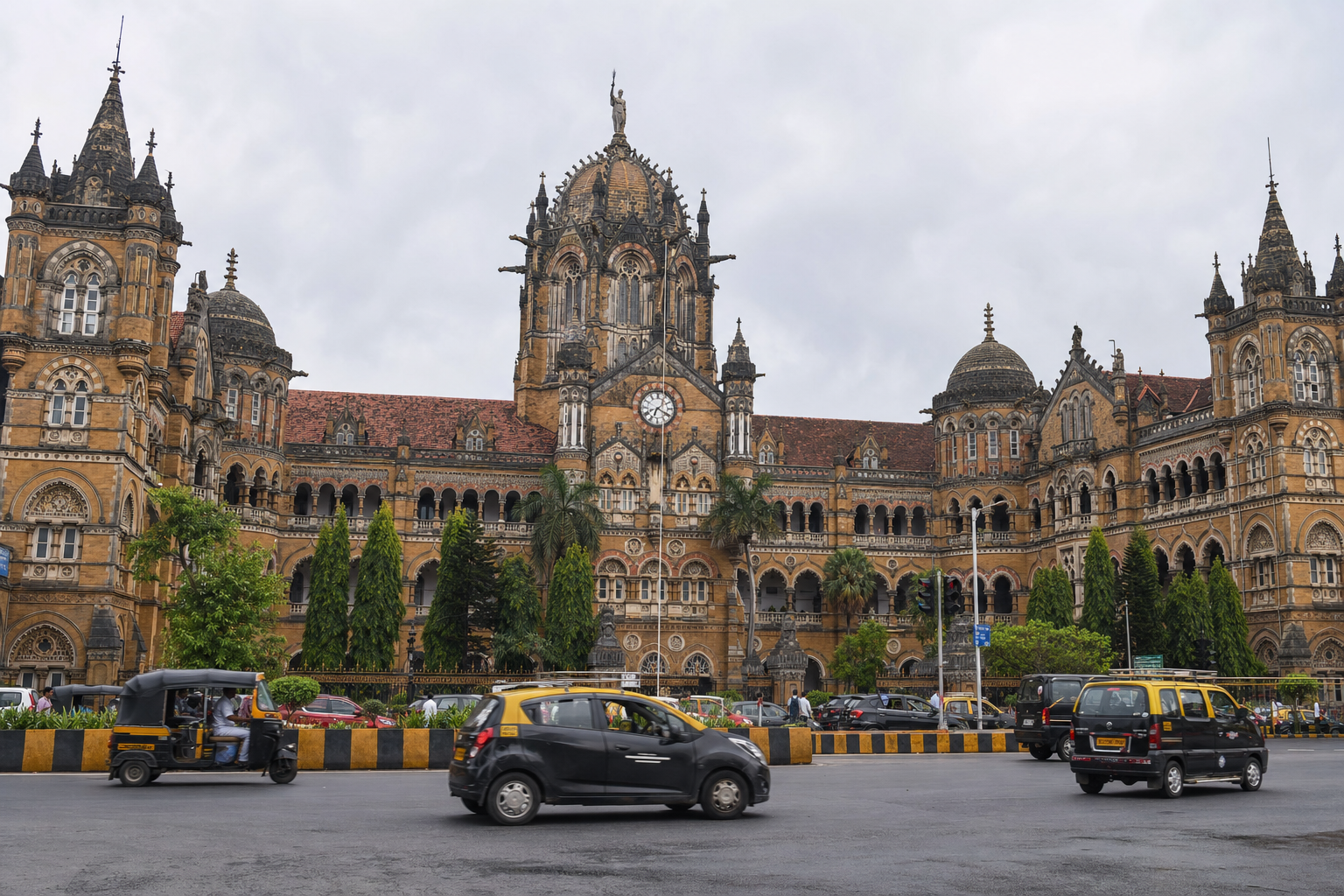 Ground-level photograph of Chhatrapati Shivaji Maharaj Terminus (CSMT) taken from across the street, showcasing its Victorian Gothic facade and Mumbai city traffic in the foreground